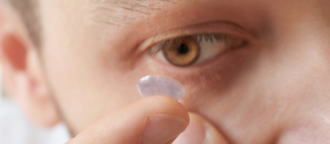 Young man putting contact lens in his eye, closeup